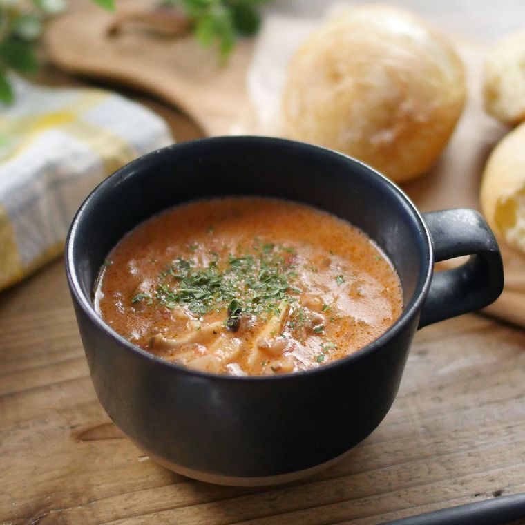 片手の黒いマグカップに盛りつけられたチーズとトマトのミルクスープ