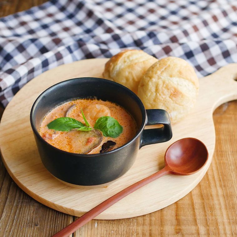 片手の黒いマグカップに盛りつけられたえびのトマトクリームスープ