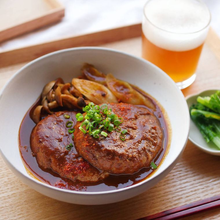 白い器に盛られたさばと豆腐の味噌ハンバーグに飲み物と副菜が添えられている様子