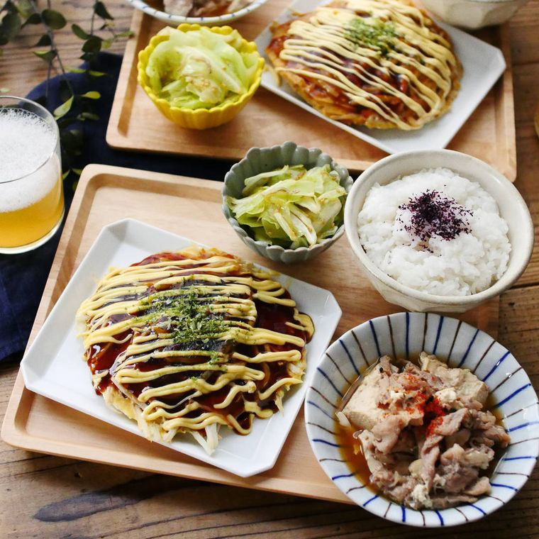 木製の四角いお盆に並べられたお好み焼きとごはん、おかずなど