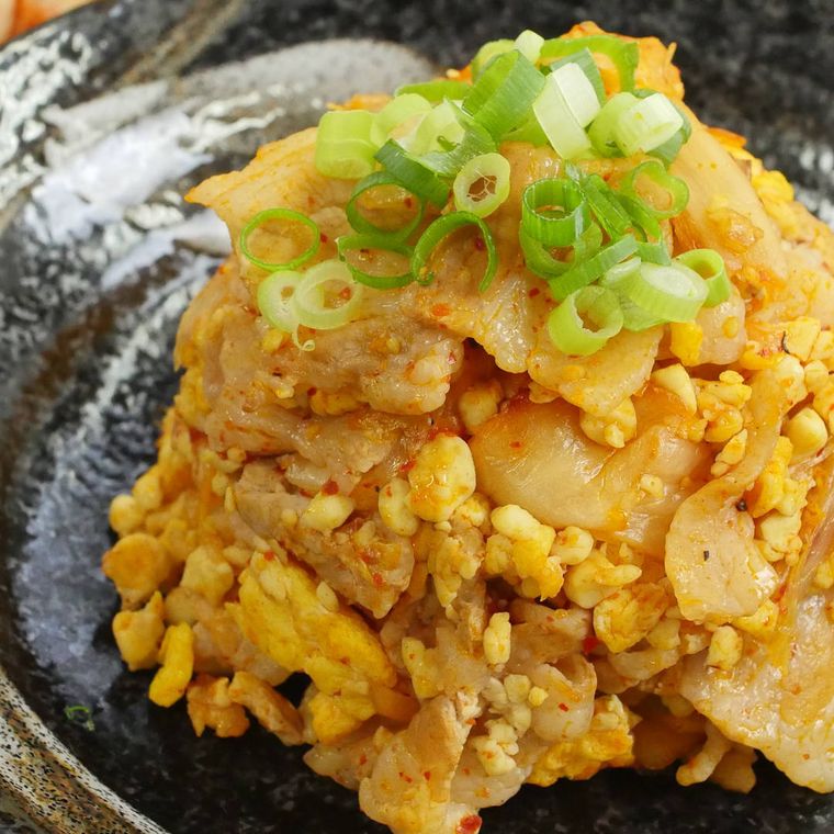 黒い丸皿に盛り付けた、ねぎがトッピングされている豚キムチ豆腐チャーハン