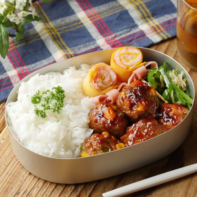 銀の弁当箱に入っているミートボールとごはん、キャンディー型の卵焼き