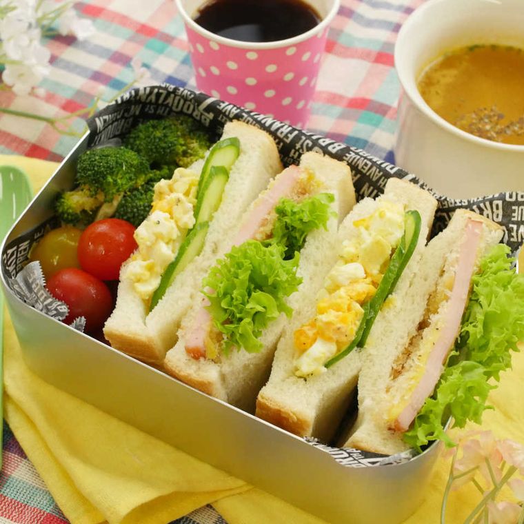銀のお弁当箱に詰められている卵とハムカツのサンドイッチと野菜