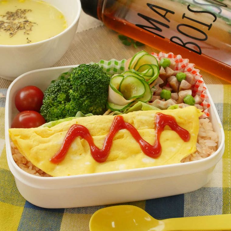 白い弁当箱に詰められているオムライスと野菜