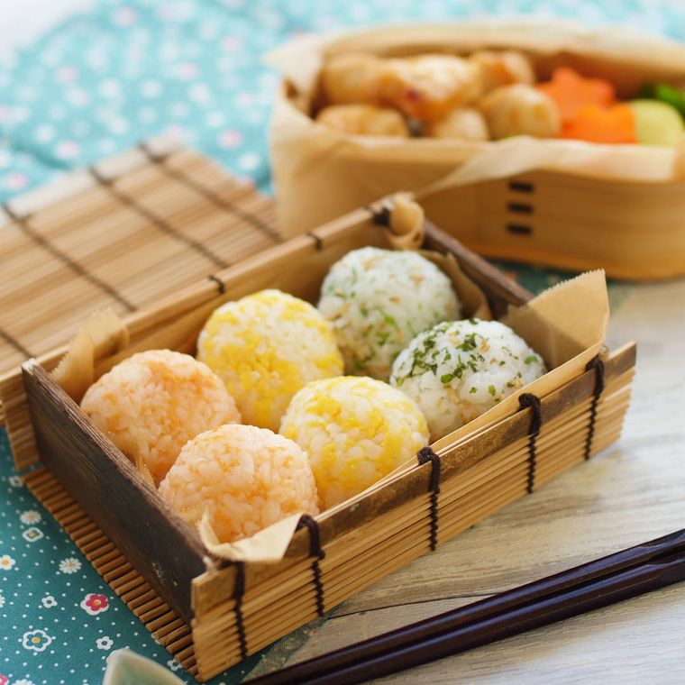 茶色い弁当箱に詰められている色とりどりのおにぎりとおかず