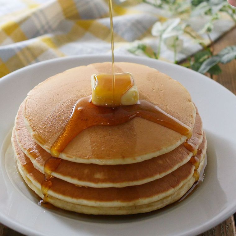白い皿に盛りつけられたホットケーキにシロップをかけている様子