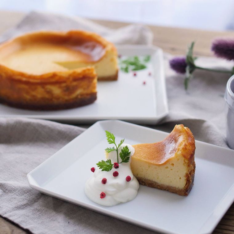 白く四角い皿にカットして生クリームを添えた、基本のベイクドチーズケーキ