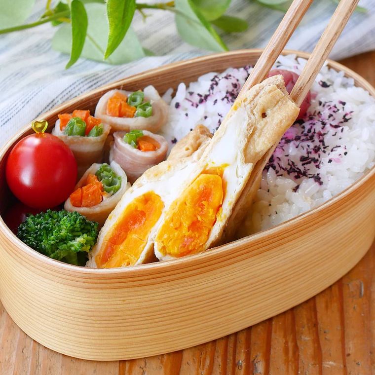 お弁当箱に入った甘辛卵巾着を箸でつまんでいる様子