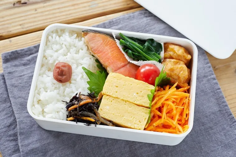 白いお弁当箱に焼鮭や卵焼きが詰められている