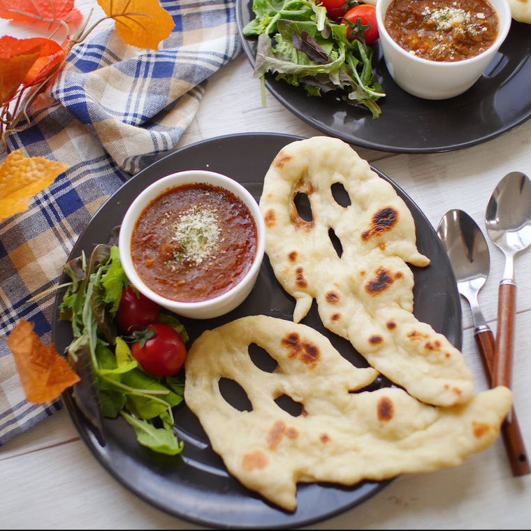 黒い丸皿に盛られたおばけナンとココット型に入ったカレー、ベビーリーフ、ミニトマト