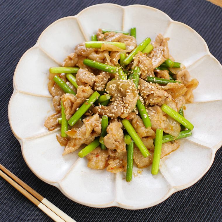白い花の形の皿にのせられた豚肉とにんにくの芽炒め