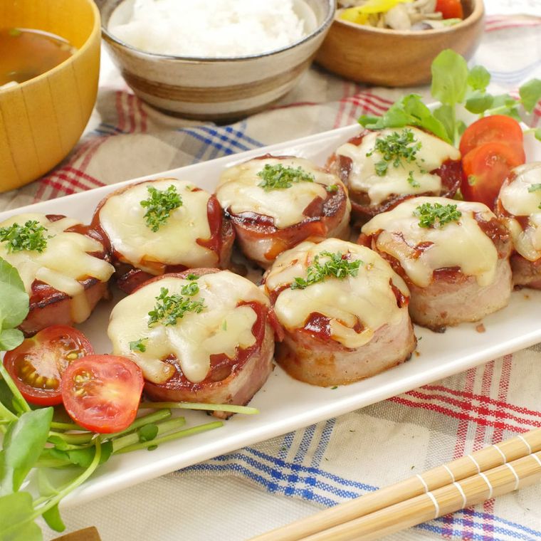 白い長皿に盛りつけられているベーコン巻きハンバーグ