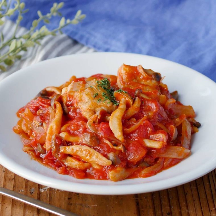 鶏肉とトマトソースが絡んだ鶏肉のトマト煮込みが白い円形の洋食器に盛り付けられているところ