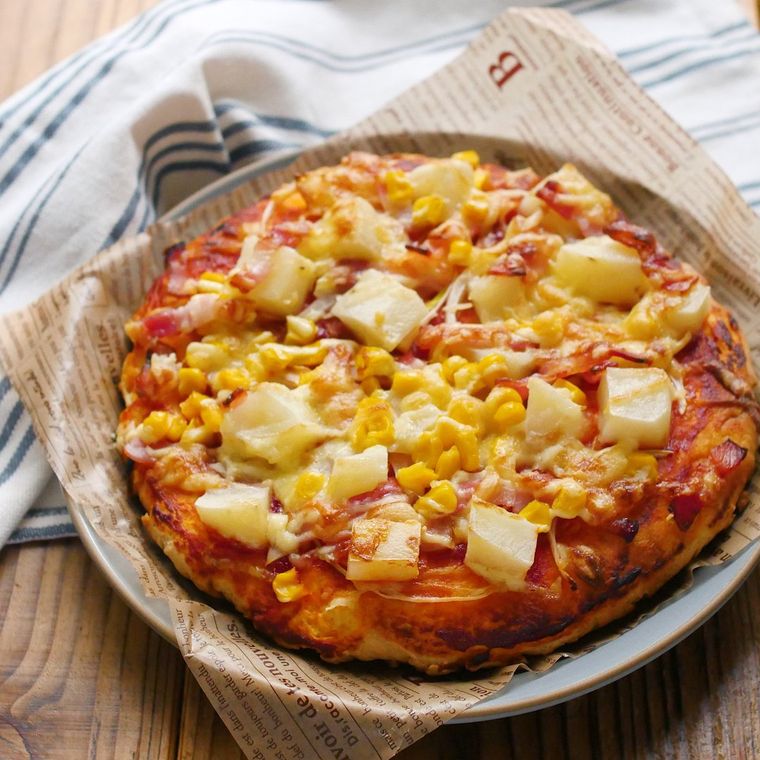 ホットケーキミックスで作ったピザ生地にじゃがいも、ベーコン、コーンがのったピザがグレーの皿の上に焼きあがったところ