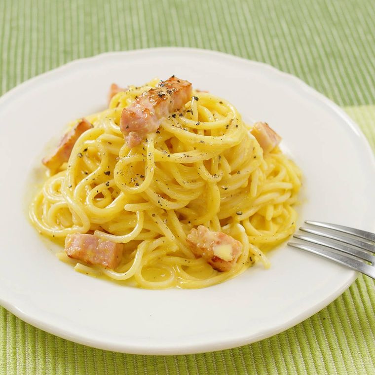 太めのパスタにクリーミーなソースが絡んだカルボナーラが白いパスタ皿に盛り付けられているところ