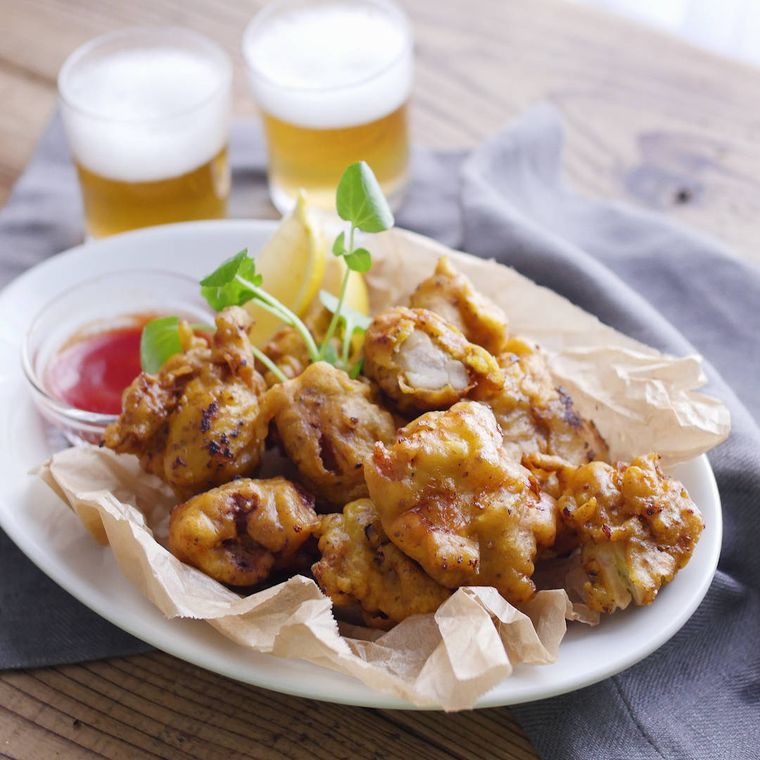 マスタードとカレー風味のチキンフリットがレモンと一緒に白い楕円形の皿に盛り付けられているところ