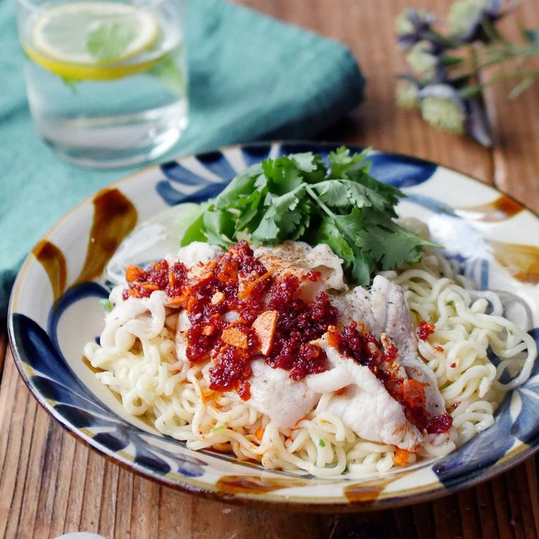 模様付き皿に盛りつけられた豚バラ肉とパクチーのピリ辛あえ麺