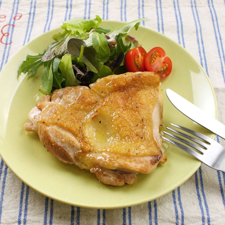 緑色の皿に盛られたチキンのソテーに野菜が添えてある様子