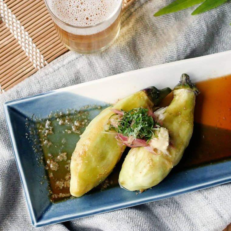 紺色の柄が入った白い皿に盛り付けられた蒸しなすのごまポンがけ