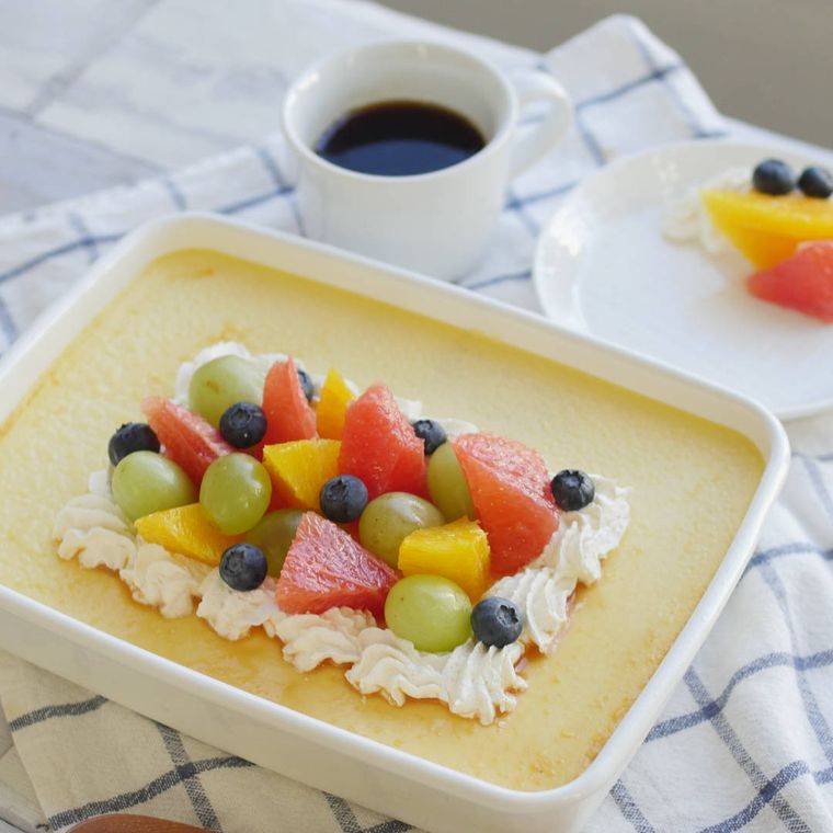 白いホーロー保存容器にフルーツと生クリームをトッピングしたカスタードプリンが盛られている様子