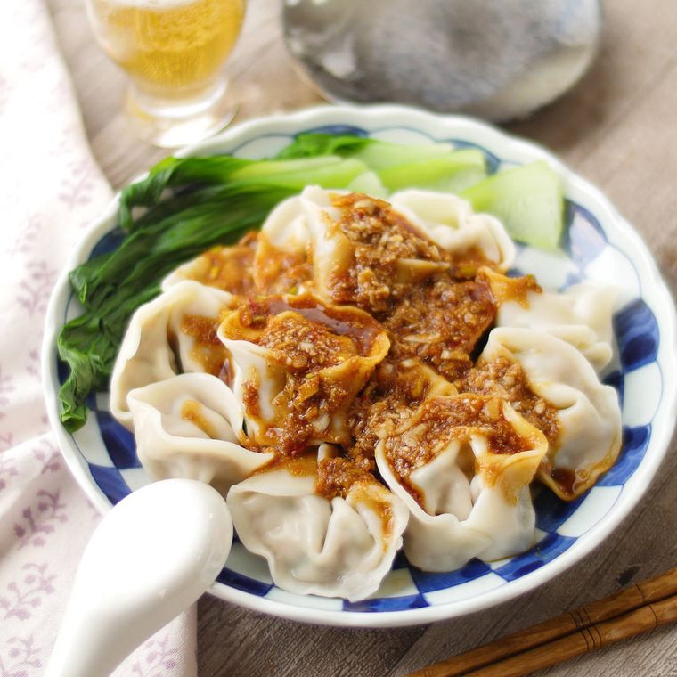 白と青色の格子柄皿に盛りつけられているごまダレがけの水餃子