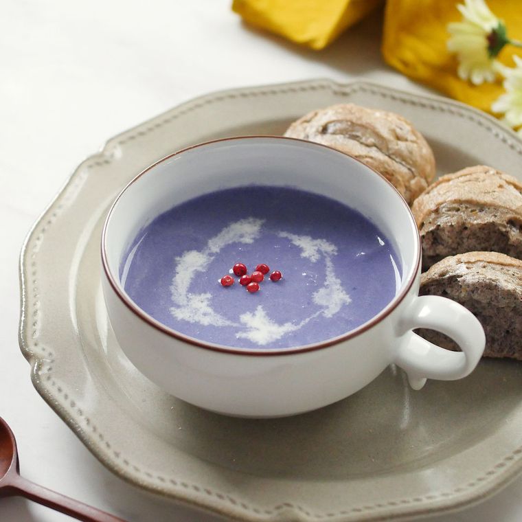 ソーサーの上のスープカップに入っている紫キャベツのクリームスープ