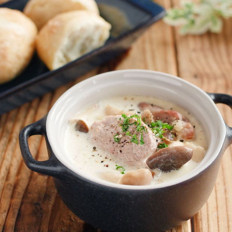 黒い器に盛られた、豚ヒレ肉ときのこのクリームスープと並べられたパン