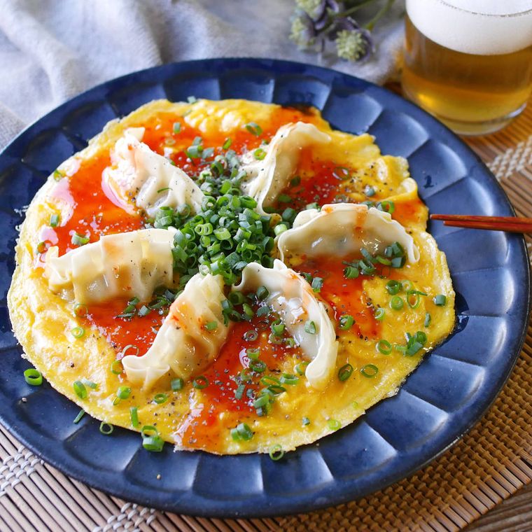 紺色の皿に入った、餃子をのせたオープンオムレツ