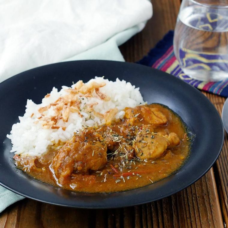 黒色の皿に盛られたトマトとチキンのスパイスカレー