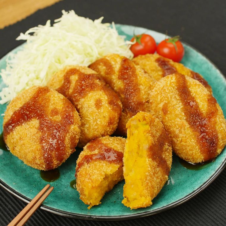 千切りキャベツとミニトマトを添えた緑の皿に盛られた、かぼちゃコロッケ