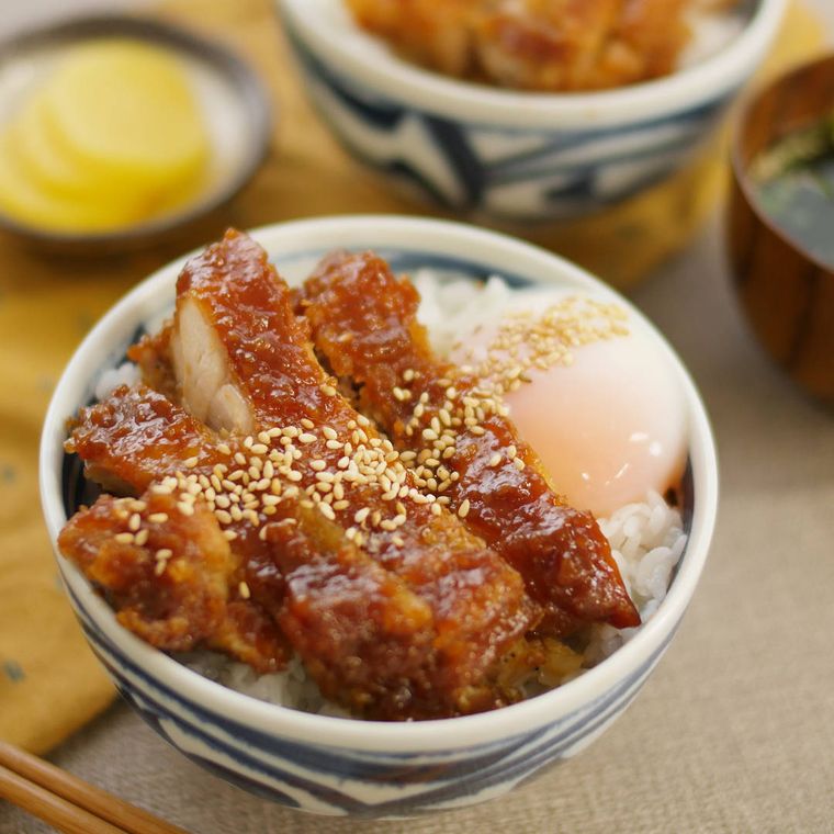 白地に青い模様入りの丼に盛られ、白いりごまと温泉卵をトッピングした、みそだれの鶏竜田揚げ丼