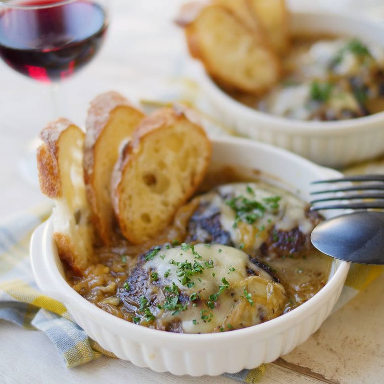 白い器に盛られたオニオングラタン煮込みハンバーグとカットされたパン