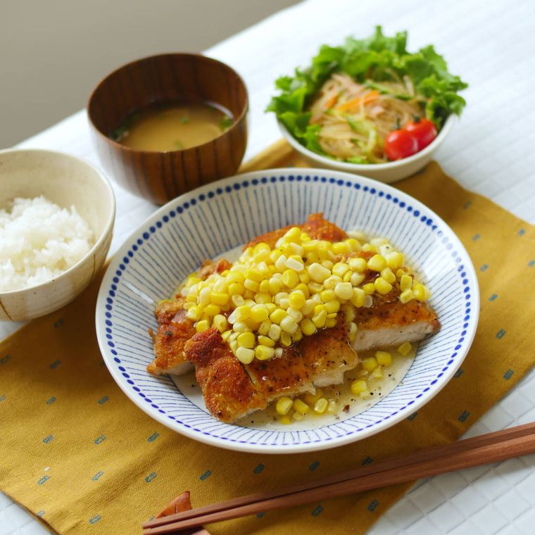 グリルチキンにコーンがのった料理とサラダとごはんとみそ汁