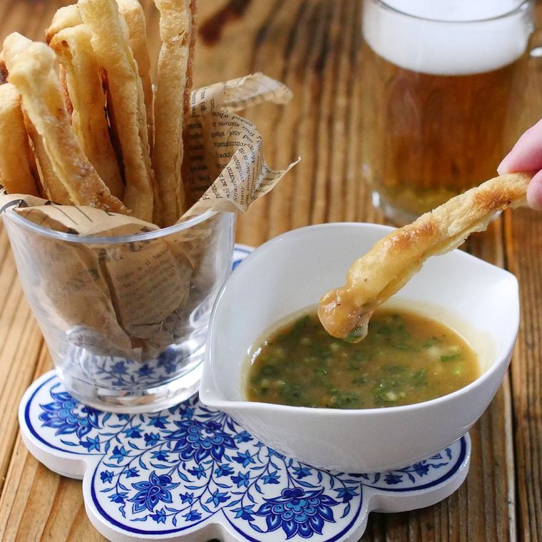 透明なグラスに入った油揚げスティックを1本つまみ、たれにつけている様子