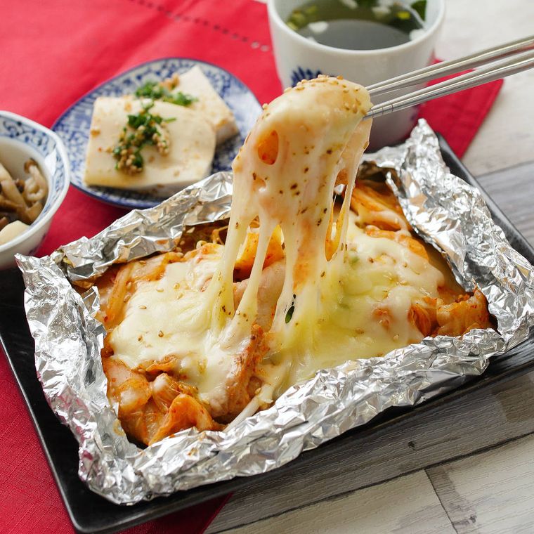 黒い角皿に盛り付けたチーズ豚キムチのホイル焼きを箸で持ち上げる様子