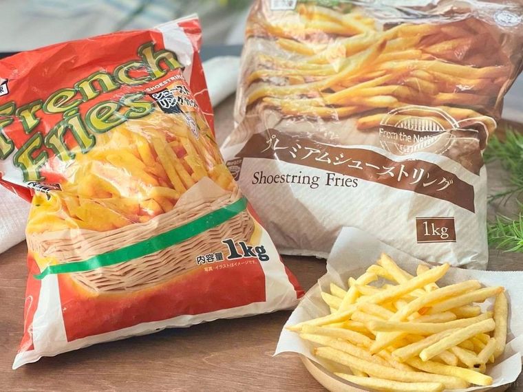 大袋に入った冷凍フライドポテト2袋と、木のトレーに盛られたフライトポテトが、木のテーブルに置かれている