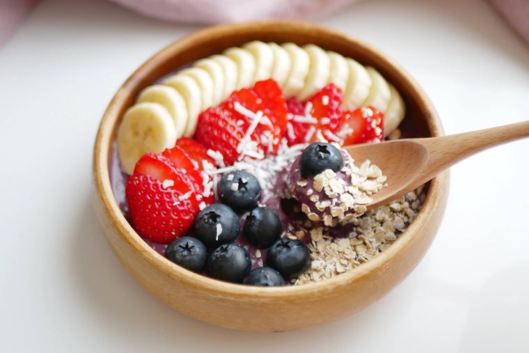 木の器に入ったアサイーボウルを木のスプーンですくう様子