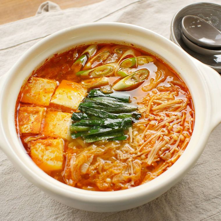 白い両手鍋に入っている豚バラ肉とえのき、豆腐などのキムチ鍋