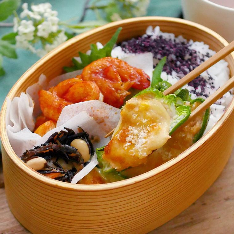 お弁当箱に入ったツナマヨピーマンカップのピザを箸でつまんでいる様子