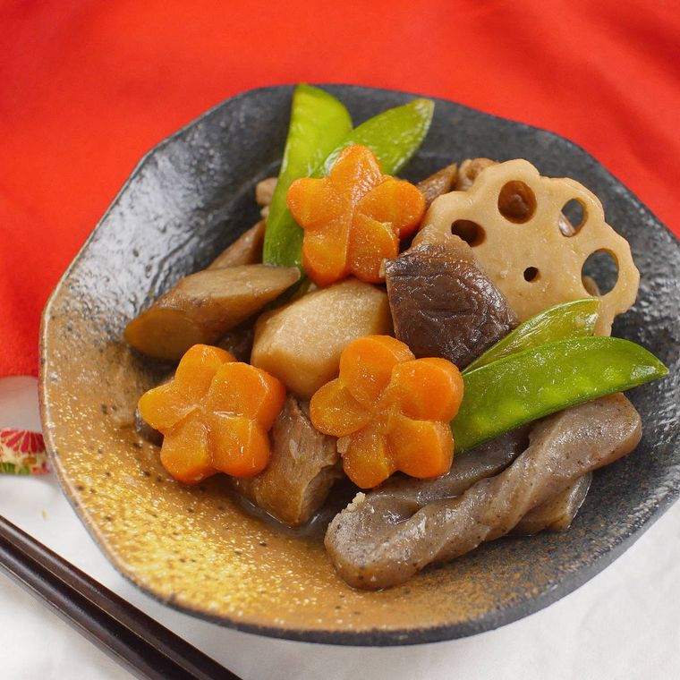 黒と金の器に盛られたれんこんとこんにゃく入り筑前煮