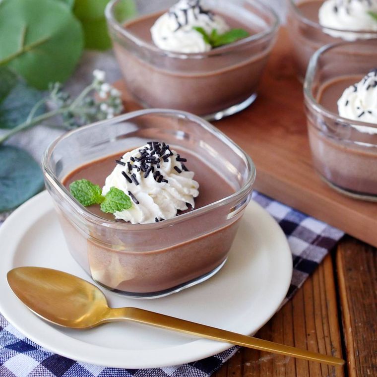 透明のグラスに入ったチョコプリンが白い皿に置かれている様子
