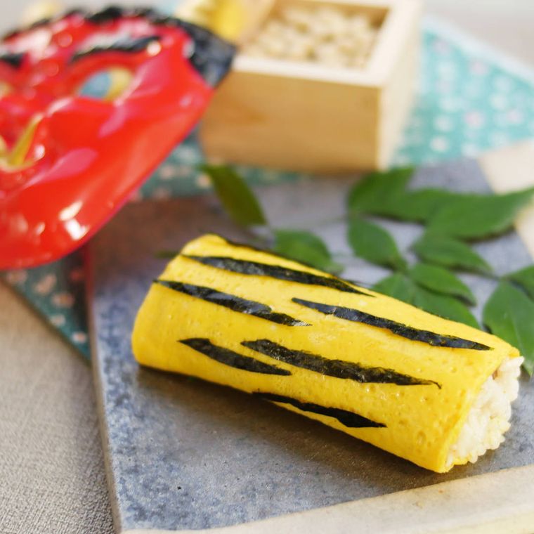 角皿に盛りつけられた虎柄の甘辛チキン恵方巻き、豆や鬼の面など