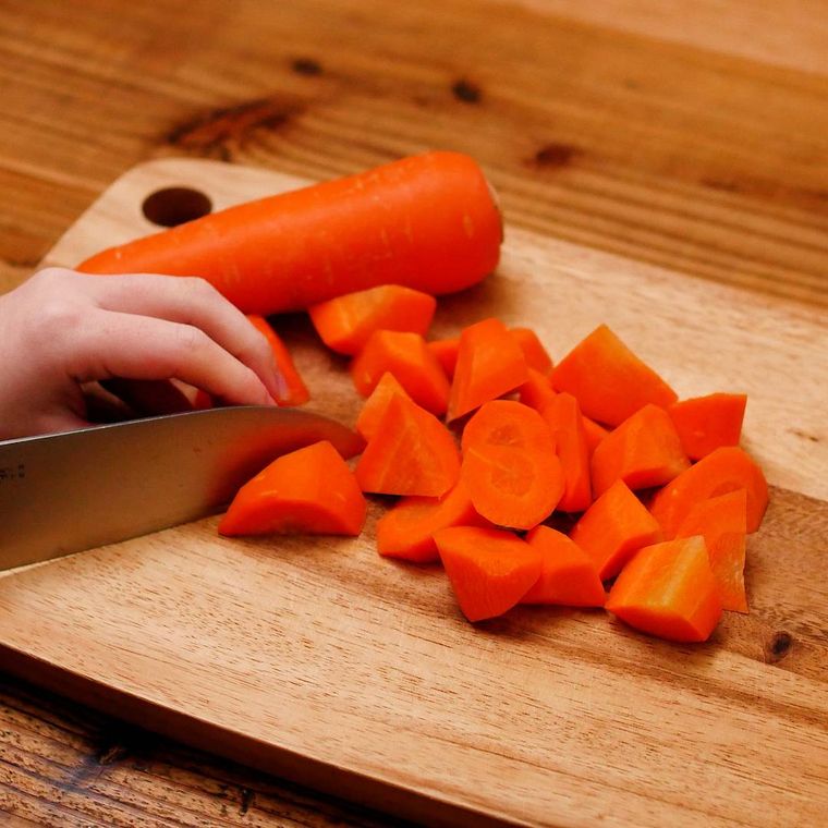 木製のまな板の上でにんじんを切っている様子