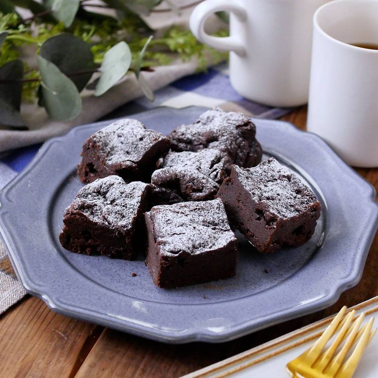 青地に縁付きの丸皿に盛られ、粉砂糖をトッピングしたビターチョコレートケーキ