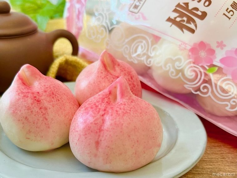 グレーの皿の上に業務スーパーの桃まんじゅうが3個置かれ、その奥には桃まんじゅうが入った袋と、茶色い急須が置かれている