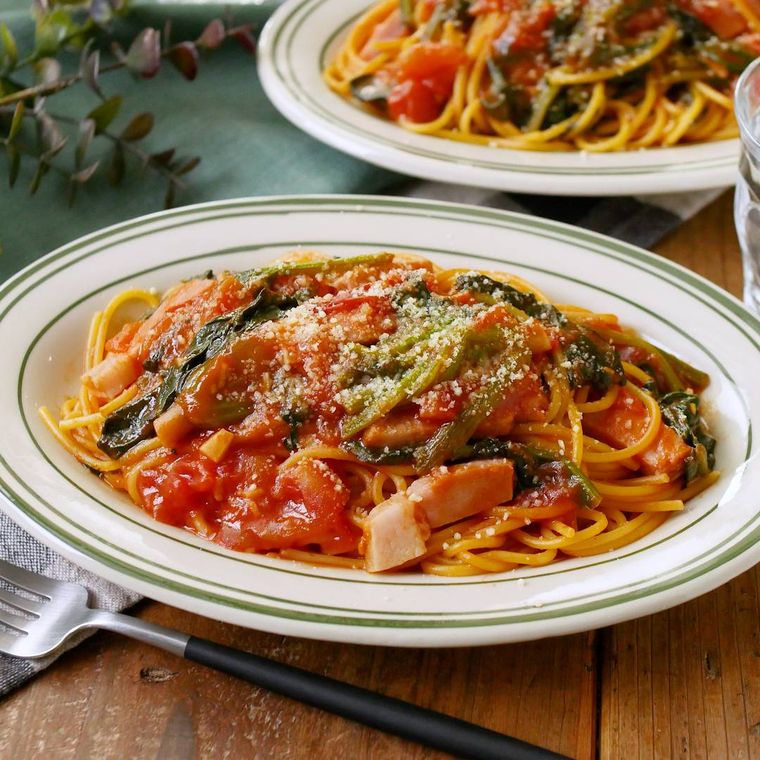 楕円形の皿に盛りつけられたほうれん草とベーコンのトマトパスタ