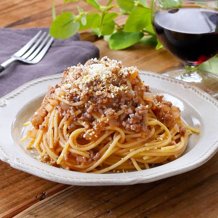白い皿に盛り付けたボロネーゼ風パスタと赤ワイン