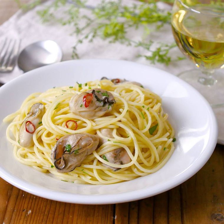 白い皿に盛りつけられた牡蠣のオイルパスタにスプーンとフォークが添えられている