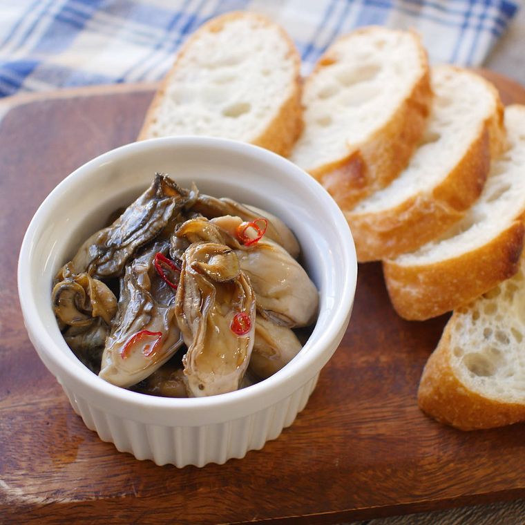 器に盛りつけられた牡蠣のオイル漬けにフランスパンが添えられている