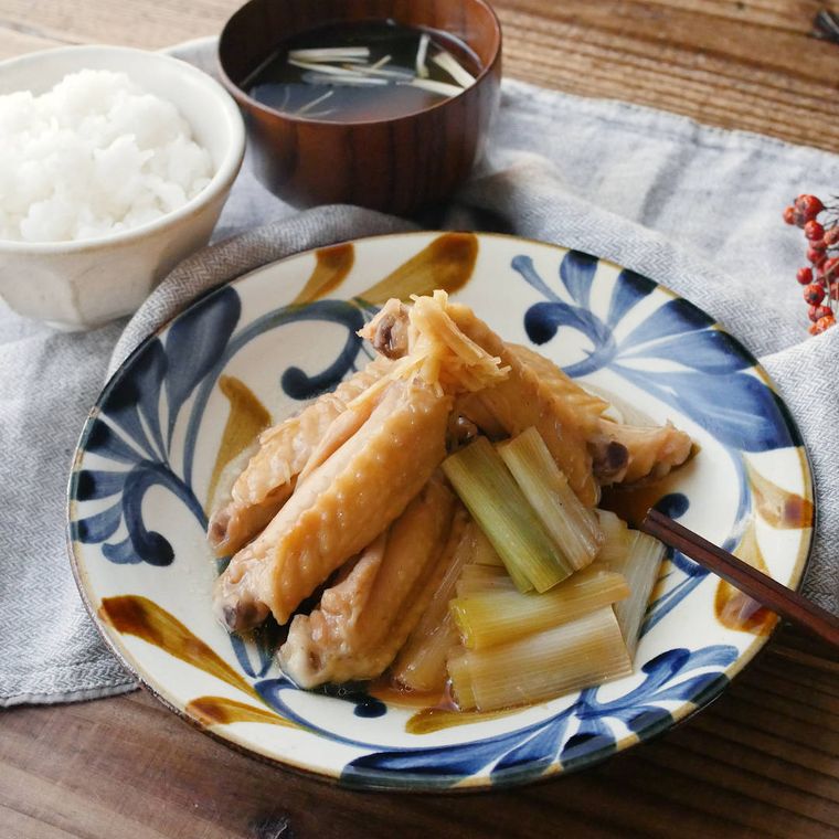 青色や茶色の模様が入った皿に盛られた鶏手羽中と長ねぎの甘辛煮